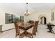 Open dining area with wood table and six chairs under chandelier next to large window and arched doorway at 18584 Alphonse Cir, Port Charlotte, FL 33948