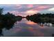 Serene water view reflecting a colorful sunset, surrounded by lush greenery and dock structures at 4053 Joseph St, Port Charlotte, FL 33948