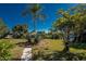 Front yard showcasing lush greenery, palm trees, and a stone paver walkway on a sunny day at 4438 Meager Cir, Port Charlotte, FL 33948