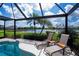 Screened-in pool area with two lounge chairs overlooking a serene lake and lush landscaping at 5733 White Jasmine Way, North Port, FL 34287