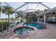 Screened-in pool and spa area featuring a built-in outdoor kitchen, lush landscaping, and serene water views at 1091 Rotonda Cir, Rotonda West, FL 33947
