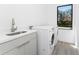 Laundry room with front loading washer and dryer and stainless steel sink next to a large window at 24294 Santa Inez Rd, Punta Gorda, FL 33955