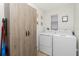 Well-lit laundry room with white washer and dryer, wood cabinet and small window at 2903 Pope St, North Port, FL 34287