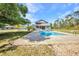 Spacious backyard with pool, patio, Tiki hut, and mature trees on a sunny day at 29324 Leah Rd, Punta Gorda, FL 33982
