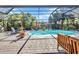View of an enclosed pool area that includes lounge chairs, tropical plants, and brick patio at 1357 Le Pera Rd, Englewood, FL 34223