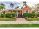 Charming peach home featuring a welcoming front porch, brick walkway, and lush tropical landscaping at 114 Mcgregor St, Punta Gorda, FL 33950