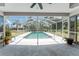 View of a screened-in pool with clear water and surrounding patio, lush landscaping, and ceiling fan in the covered area at 1173 Belmar Ave, Port Charlotte, FL 33948