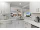 Well lit kitchen sink with white cabinetry, white marble countertop and view to living room at 3480 Pinetree St, Port Charlotte, FL 33952