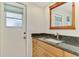 A well-lit bathroom with granite countertops, wood cabinets, a decorative mirror, and direct access to the exterior at 452 Greenwich Nw Ave, Port Charlotte, FL 33952