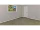 A simple bedroom with a large window, neutral-toned carpet, and a door at 452 Greenwich Nw Ave, Port Charlotte, FL 33952