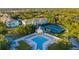 Aerial view of a community pool, tennis courts, and buildings surrounded by lush landscaping and mature trees at 19375 Water Oak Dr # 106, Port Charlotte, FL 33948