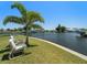Relaxing waterfront backyard featuring lush grass, a swaying palm tree, and comfortable seating for enjoying the peaceful view at 21444 Higgs Dr, Port Charlotte, FL 33952