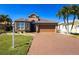 Beautiful house with a brick driveway, lush green lawn, and lovely palm trees against a clear blue sky at 10227 Windsong Rd, Punta Gorda, FL 33955