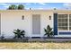 Well-maintained home featuring white exterior, blue shutters, tropical plants, and a decorative screen door at 18263 Ohara Dr, Port Charlotte, FL 33948