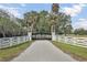 Private driveway with automatic gate entrance, white fencing, and mature palm trees offer a grand welcome at 7200 Riverside Dr, Punta Gorda, FL 33982