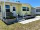 Charming yellow mobile home exterior with gray trim and brick accent, complemented by green foliage at 805 S Green Cir, Venice, FL 34285