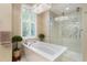 A standalone tub sits next to a window and glass shower, with plants adding a vibrant touch at 13761 Long Lake Ln, Port Charlotte, FL 33953