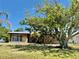 Charming single-story home featuring a stone facade, mature trees, and lush green lawn at 261 Caddy Rd, Rotonda West, FL 33947