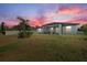 View of backyard at sunset, featuring a covered patio, privacy fence, and well-manicured lawn at 3544 Monfero Ave, North Port, FL 34286