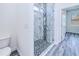 Tiled shower featuring mosaic floor and glass enclosure, leading to the toilet and grey wood-style flooring at 4285 Oak Terrace Cir, Port Charlotte, FL 33953