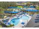 Aerial view of the community pool with tennis courts, a playground, blue umbrellas, and lounge chairs at 1215 Jonah Dr, North Port, FL 34289