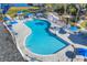 Aerial view of an oddly shaped community pool with a hot tub, lounge chairs, and umbrellas on a large paved deck at 1215 Jonah Dr, North Port, FL 34289