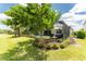 Green backyard with tree and manicured bushes with view of the back of the house and screened-in pool at 17924 Corkwood Bend Trl, Punta Gorda, FL 33982