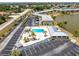 Aerial view of a community pool with lounge chairs, umbrellas, palm trees, a parking area, and fenced enclosure at 25225 Rampart Blvd # 1603, Punta Gorda, FL 33983