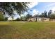 View of the back of the home with a large yard, screened porch, and mature trees at 30154 Beech Rd, Punta Gorda, FL 33982