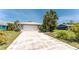 Exterior shot showcasing driveway and lush palm trees, complemented by a light gray house with a white garage door at 2008 Pellam Blvd, Port Charlotte, FL 33948