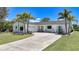 Inviting single-story home featuring a circular driveway, lush lawn, tropical trees, and attached garage at 16615 Acapulco Rd, Punta Gorda, FL 33955