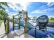 This boat sits above the water on a boat lift extending from a wooden dock in a waterfront backyard under a sunny sky at 192 Danforth S Dr, Port Charlotte, FL 33980