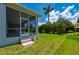 Well-maintained backyard featuring lush green grass, tropical foliage, and a screened-in lanai with steps at 3302 Palm Dr, Punta Gorda, FL 33950