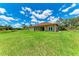 Spacious green backyard with lush lawn and a view of a well-maintained tan-colored home under a blue sky with white clouds at 4380 Maddock Cir, North Port, FL 34286