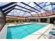 Serene pool area featuring a large screened enclosure, patio furniture, lush landscaping, and clear blue water at 13295 Eisenhower Dr, Port Charlotte, FL 33953