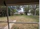 View of the serene backyard from a screened-in porch, showcasing mature trees and ample space for outdoor activities at 4205 Simkins Ave, North Port, FL 34286