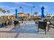 Outdoor community amenity area with tables, umbrellas and chairs near a tennis court with lush landscaping at 99 Vivante Blvd # 303, Punta Gorda, FL 33950