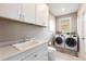 Convenient laundry room featuring modern washer and dryer, ample storage cabinets, sink, and a window for natural light at 523 Saint Girons Ct, Punta Gorda, FL 33950