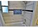 Updated bathroom features a bathtub, shower with wood-look tile, a niche, and a window for natural light at 107 Sinclair Se St, Port Charlotte, FL 33952