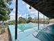View of the pool and covered pool deck with a green cover, along with lush landscaping in the background at 1611 Robbins Rd, Nokomis, FL 34275