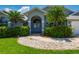 Charming home entrance featuring a beautifully landscaped yard, tropical palm trees, and an elegant arched double-door entry at 25371 Paladin Ln, Punta Gorda, FL 33983