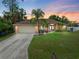 Charming single-story home featuring an attached two car garage, and lush landscaping under a colorful sunset at 2373 Chartwell Ave, North Port, FL 34288