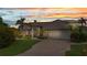 Charming home features a manicured lawn, brick driveway, mature landscaping, and a two-car garage, with a colorful sunset backdrop at 250 Freeport Ct, Punta Gorda, FL 33950