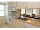 Well-lit kitchen featuring white appliances, a double sink, and a view into the dining room at 6689 Gasparilla Pines Blvd, Englewood, FL 34224