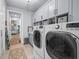 Modern laundry room featuring gray cabinetry, open shelving, and a front-load washer and dryer for convenience at 25462 Shore Dr, Punta Gorda, FL 33950