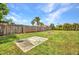 Fenced backyard with lush green grass, tropical palm trees, a concrete patio, and a charming fire pit at 457 Glenridge Nw Ave, Port Charlotte, FL 33952