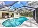 Screened-in pool area with a dining set, a pool with blue tile and green space with trees surrounding it at 6514 N Biscayne Dr, North Port, FL 34291