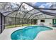 A lovely screened-in pool with a large concrete deck surrounded by a lush green space and a blue sky above at 6514 N Biscayne Dr, North Port, FL 34291