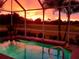 A stunning pool basks in the glow of an orange sunset with palm trees surrounding the screened lanai at 4567 Whispering Oaks Dr, North Port, FL 34287