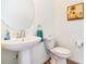 Stylish powder room with a pedestal sink, round mirror, framed tropical art, and earth-toned tiled floors at 14684 Cherry Blossom Way, Punta Gorda, FL 33955